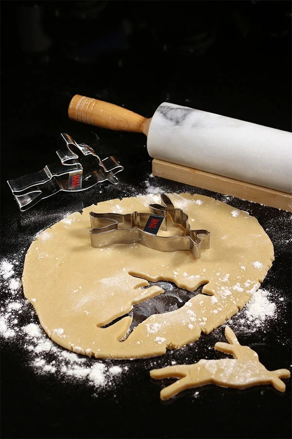 Cookie dough rolled out on a black counter top with HALL Napa Valley bunny cookie cutters on top and a marble rolling pin next to it.