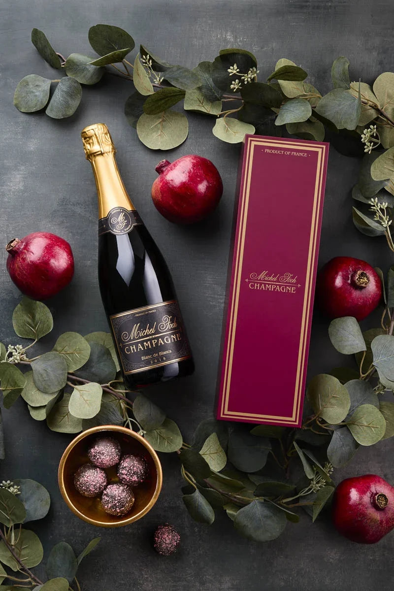 Image of the Michel Foch Blanc de Blancs 2015 holiday gift set featuring a bottle of the  Michel Foch Blanc de Blancs 2015 and an elegant branded gift box. The image is decorated with pomegranates, truffles and garland.